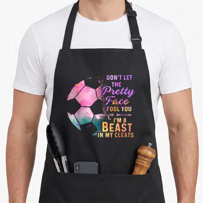 Soccer mother's apron - Watercolor soccer ball in pink purple teal orange next to stacked text reading Don't Let — shown on a black cotton canvas apron against a white background