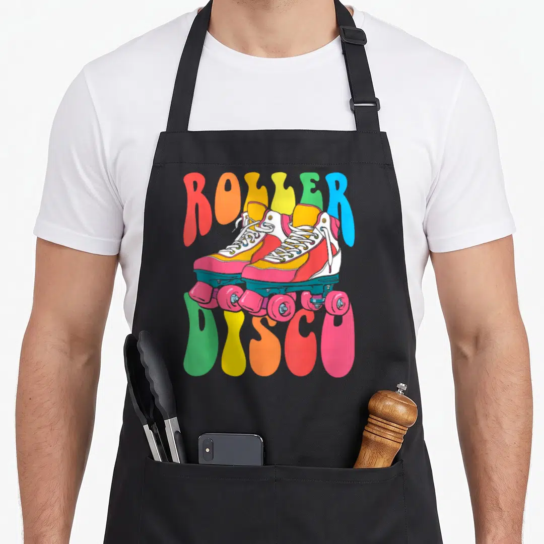 Disco seventy 70s apron - Retro quad roller skates in pink and teal with arched ROLLER DISCO text in rainbow colors — shown on a black cotton canvas apron against a white background