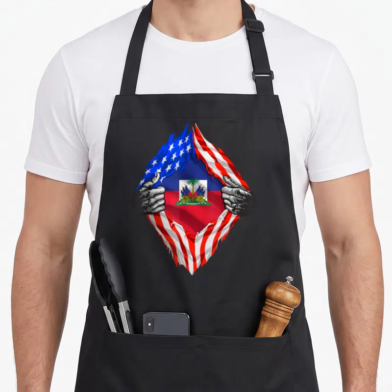 Haiti american flag apron - Two grey hands tear USA flag to reveal Haitian flag and coat of arms — shown on a black cotton canvas apron against a white background