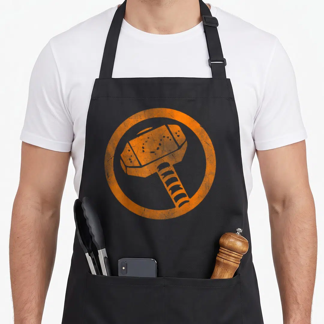 Hammer halloween apron - Stylized orange hammer centered inside a thick circular border on a black background — shown on a black cotton canvas apron against a white background