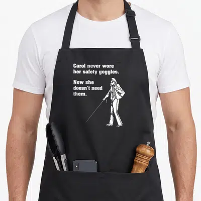 Carol safety apron - White text and blind woman with cane illustration on gray background — shown on a black cotton canvas apron against a white background