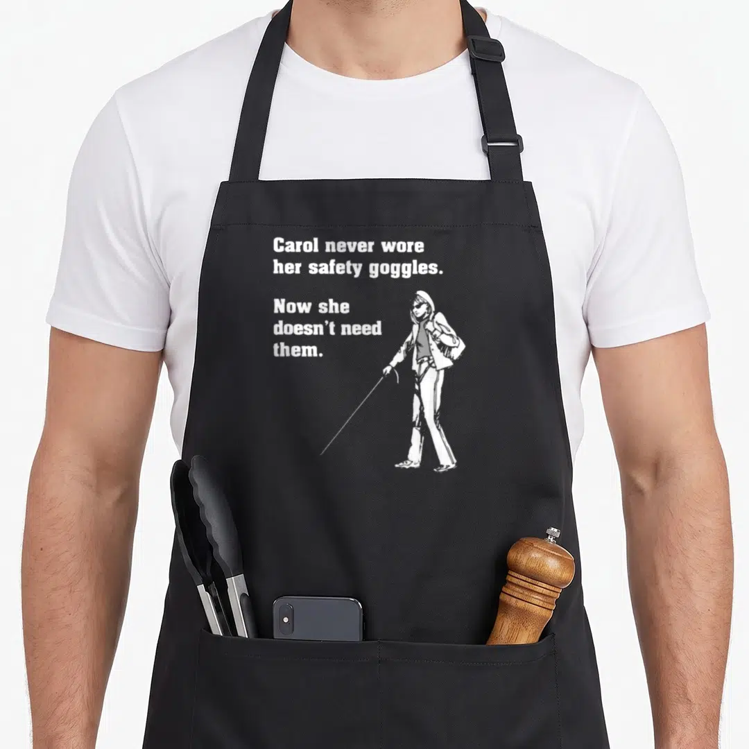 Carol safety apron - White text and blind woman with cane illustration on gray background — shown on a black cotton canvas apron against a white background