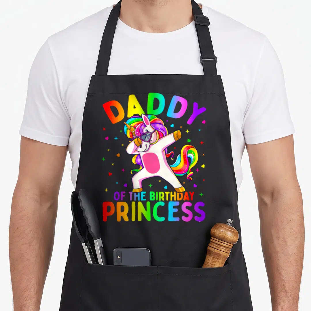 Dabbing daddy apron - Cartoon unicorn dabbing with rainbow mane and text Daddy of the Birthday Princess — shown on a black cotton canvas apron against a white background
