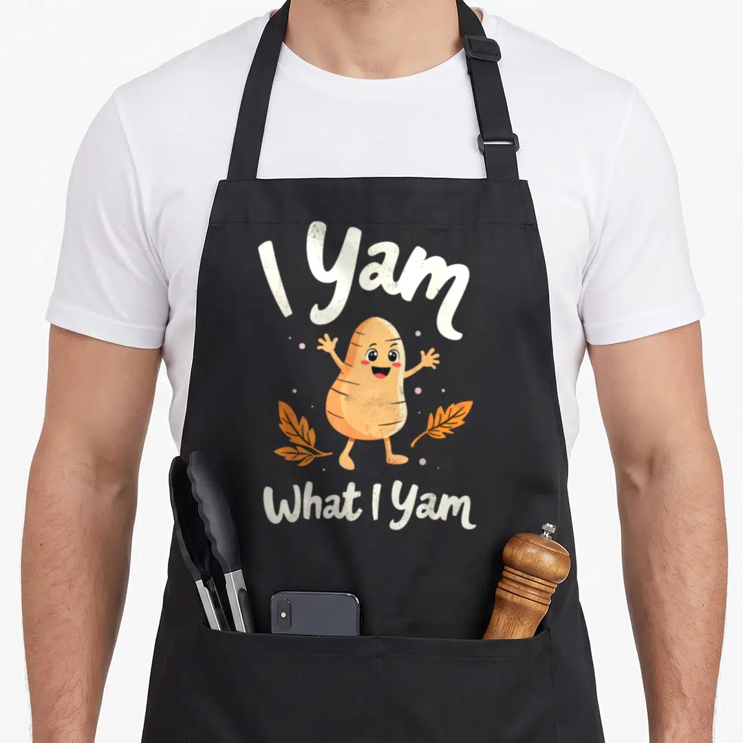 Sweet thanksgiving apron - Cartoon yam character with text I Yam What I Yam and orange leaves — shown on a black cotton canvas apron against a white background