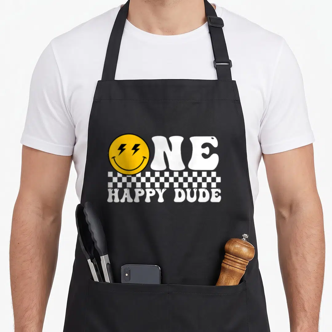 Dude family cooking aprons - Yellow smiley face with lightning eyes replacing O in ONE HAPPY DUDE text above — shown on a black cotton canvas apron against a white background