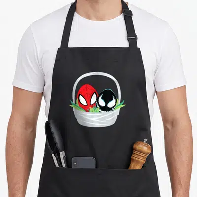 Cute easter basket apron - Red and black character eggs sitting in a white basket with green grass blades — shown on a black cotton canvas apron against a white background