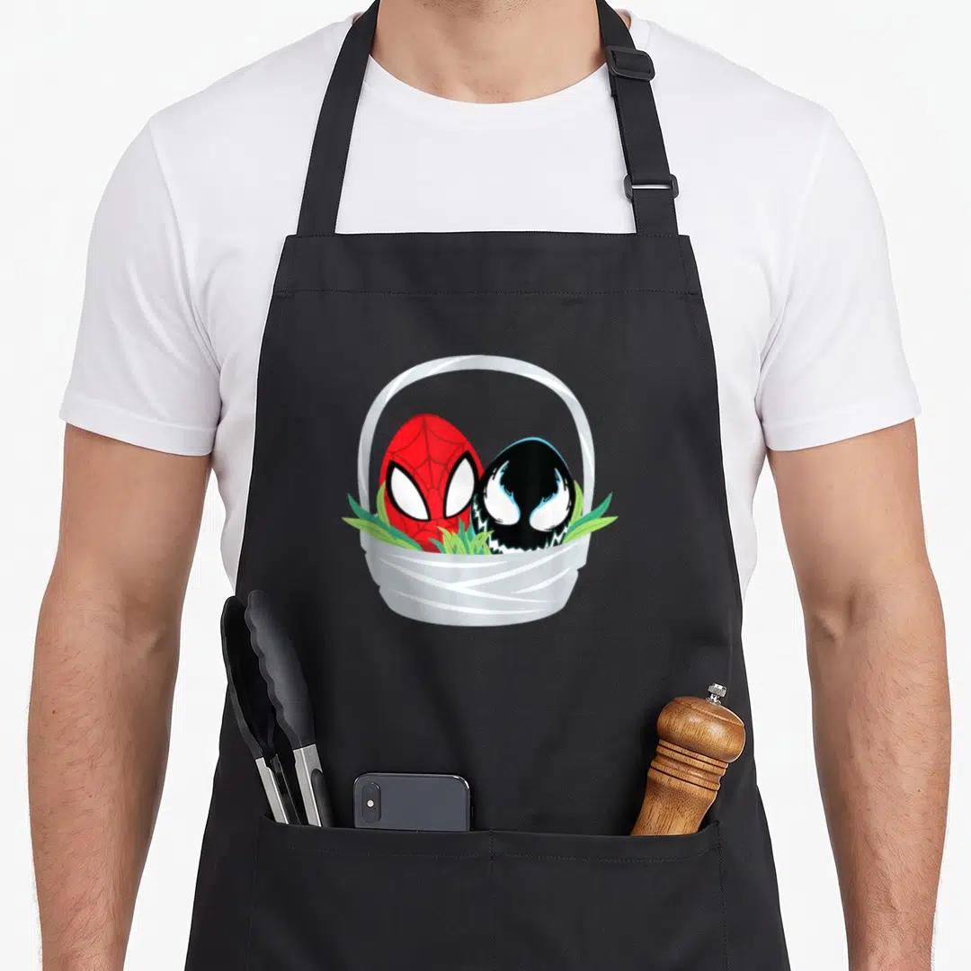 Cute easter basket apron - Red and black character eggs sitting in a white basket with green grass blades — shown on a black cotton canvas apron against a white background