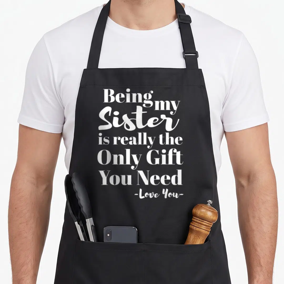 Cute sister novelty apron - White stacked text reading Being my Sister is really the Only Gift You Need on black fabric — shown on a black cotton canvas apron against a white background