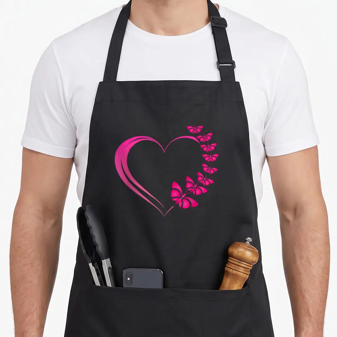 Hot butterfly apron - Pink heart outline formed by a vertical row of butterflies in a minimalist style — shown on a black cotton canvas apron against a white background