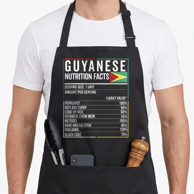 Guyanese food aprons - Nutrition facts label with Guyanese dishes and flag framed in red green yellow lines — shown on a black cotton canvas apron against a white background