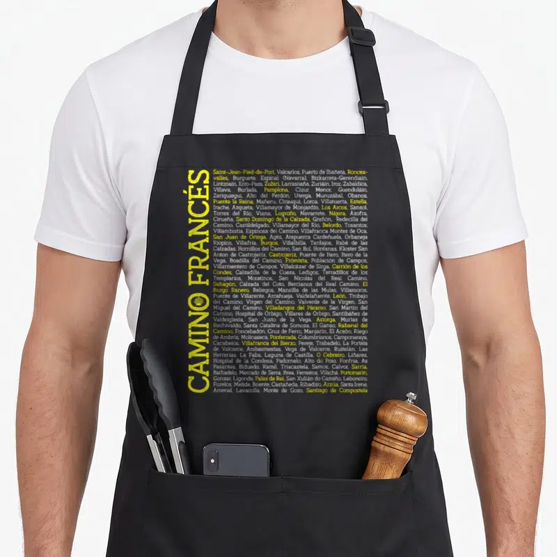 Camino scallop apron - Vertical yellow CAMINO FRANCÉS text next to list of Spanish towns and yellow scallop shell icon — shown on a black cotton canvas apron against a white background