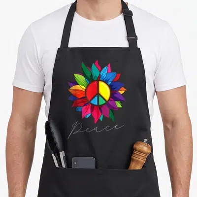 Sign sunflower apron - Multicolored flower with peace symbol and white script text — shown on a black cotton canvas apron against a white background