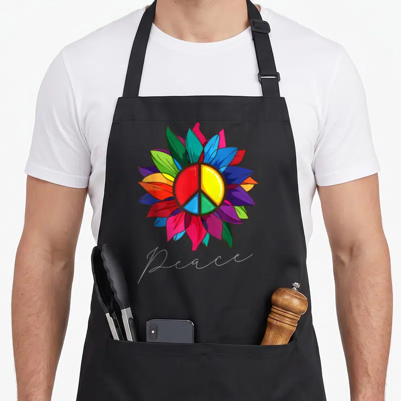 Sign sunflower apron - Multicolored flower with peace symbol and white script text — shown on a black cotton canvas apron against a white background