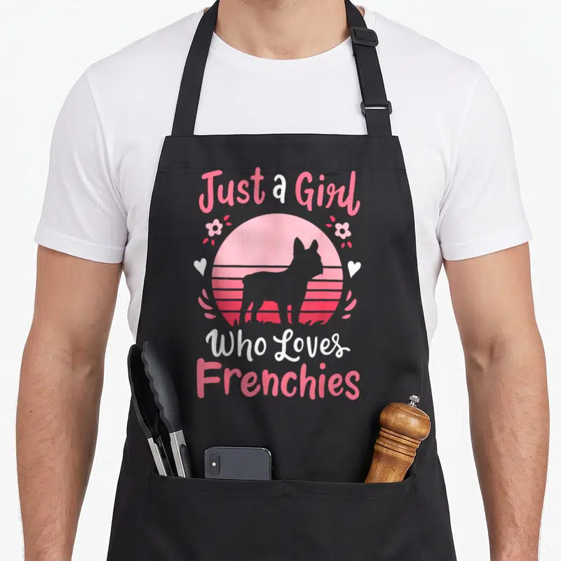 Frenchy french apron - Grey Frenchie silhouette in pink striped circle with hearts and text — shown on a black cotton canvas apron against a white background