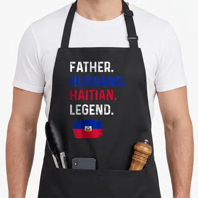 Haitian husband apron - Stacked text reading Father Husband Haitian Legend above a blue and red brush stroke flag — shown on a black cotton canvas apron against a white background