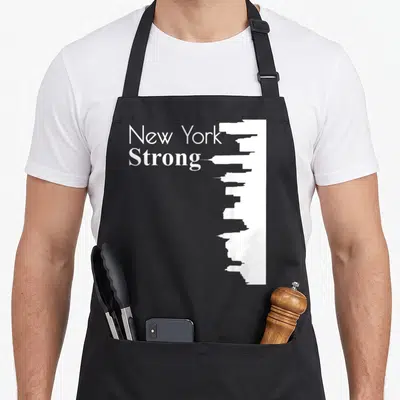 Strong new york apron - White New York Strong text next to a vertical city skyline silhouette — shown on a black cotton canvas apron against a white background