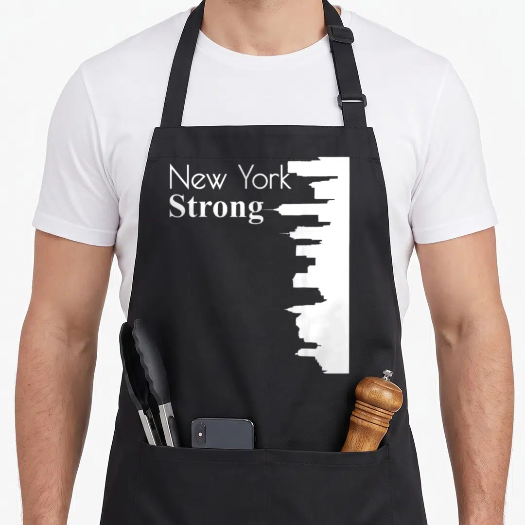 Strong new york apron - White New York Strong text next to a vertical city skyline silhouette — shown on a black cotton canvas apron against a white background