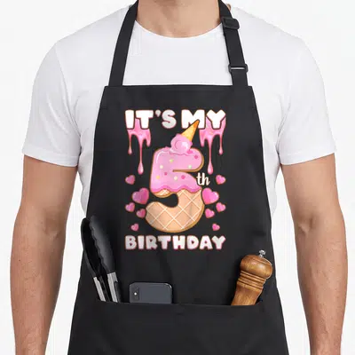 5th ice cream apron - Pink number 5 ice cream cone with IT'S MY BIRTHDAY text and scattered hearts — shown on a black cotton canvas apron against a white background