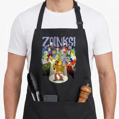 Zoink decade apron - Shaggy and Scooby-Doo under spotlight surrounded by monsters with ZOINKS! text — shown on a black cotton canvas apron against a white background