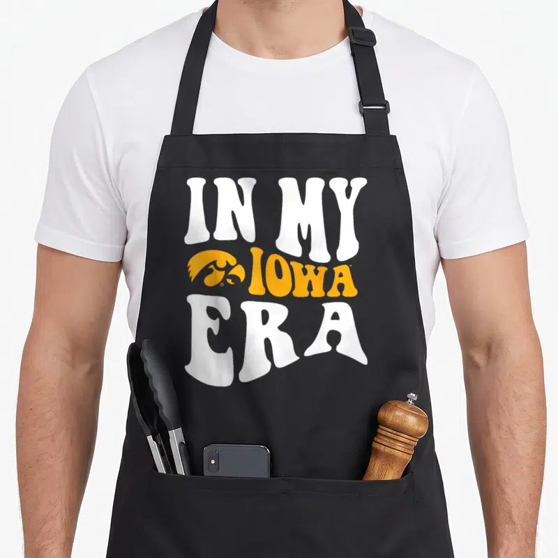Iowa hawkeyes dad apron - IN MY IOWA ERA text with yellow hawk logo and white lettering — shown on a black cotton canvas apron against a white background