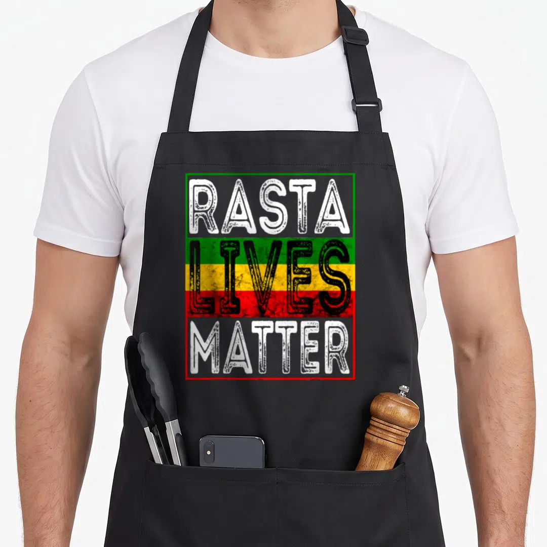 Live reggae apron - Rasta Lives Matter text in white black over green yellow red stripes inside rectangular border — shown on a black cotton canvas apron against a white background
