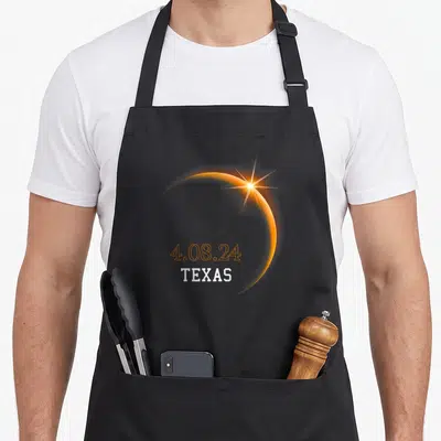 Spring texas apron - Realistic orange solar eclipse crescent with bright flare above 4.08.24 and white TEXAS text — shown on a black cotton canvas apron against a white background