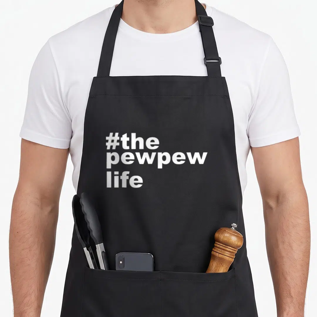 Pew husband apron - White stacked text reading #the pewpew life in bold font — shown on a black cotton canvas apron against a white background