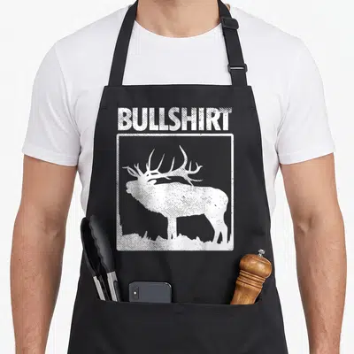Bullshirt bow apron - Distressed white text BULLSHIRT above a square frame with an elk standing on grass — shown on a black cotton canvas apron against a white background