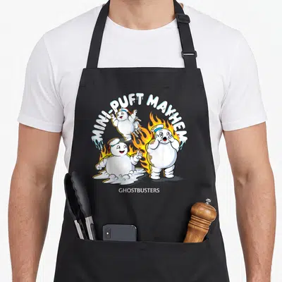 Puft animal apron - Three marshmallow characters with flames and MINI-PUFT MAYHEM text — shown on a black cotton canvas apron against a white background