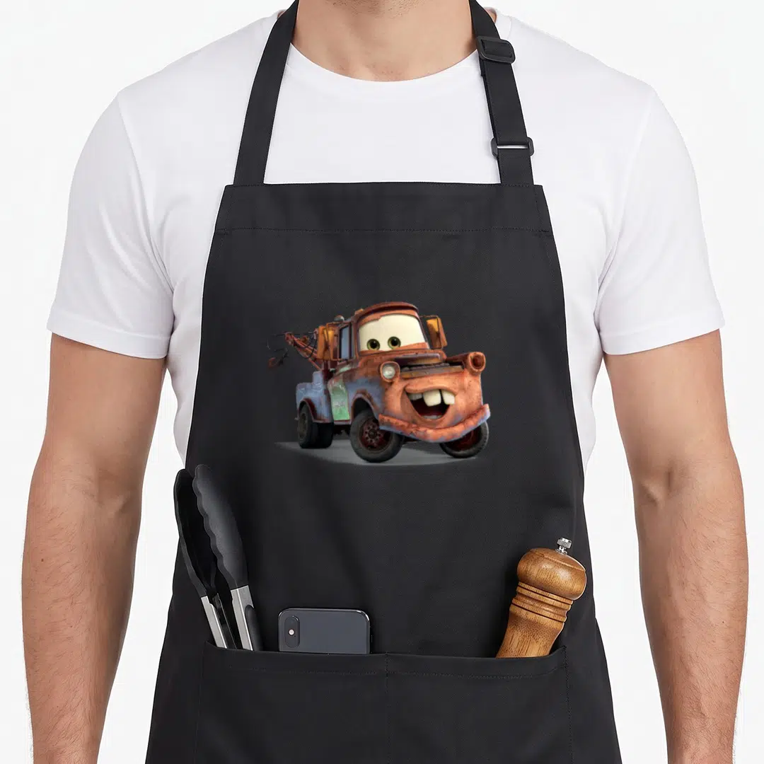 Tow mater car apron - Rusty tow truck with green eyes and buck teeth in brown and blue on grey — shown on a black cotton canvas apron against a white background