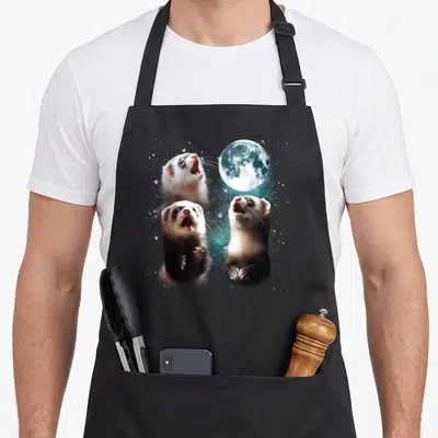Moon ferret lover apron - Three realistic ferrets with white brown and grey fur looking up at a moon among stars — shown on a black cotton canvas apron against a white background