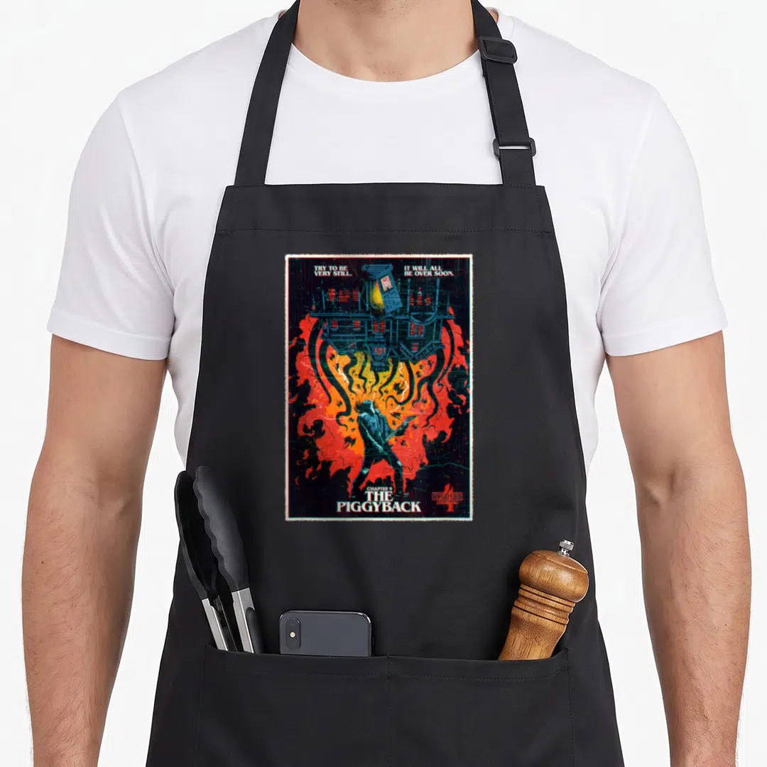 Chapter stranger apron - Eddie Munson guitar standing under upside-down Creel House with red and orange fire background — shown on a black cotton canvas apron against a white background