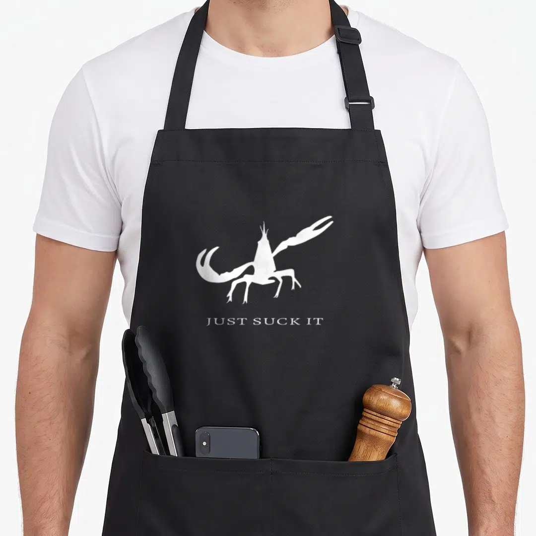 Suck crawfish apron - White lobster silhouette above text JUST SUCK IT — shown on a black cotton canvas apron against a white background