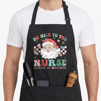 Nurse christmas santa apron - Cartoon Santa winking with stethoscope on U of NURSE, checkerboard background, scattered — shown on a black cotton canvas apron against a white background