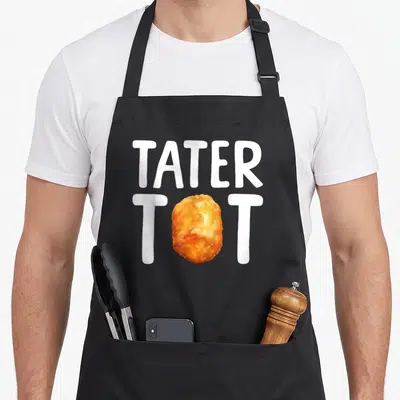 Tater tot potato apron - White TATER TOT text with golden brown tater tot replacing O on black bib — shown on a black cotton canvas apron against a white background