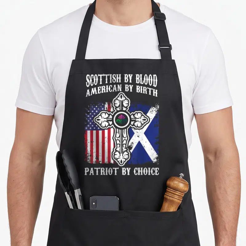 Scottish blood apron - Celtic cross with thistle over distressed US and Scottish flags with stacked text — shown on a black cotton canvas apron against a white background