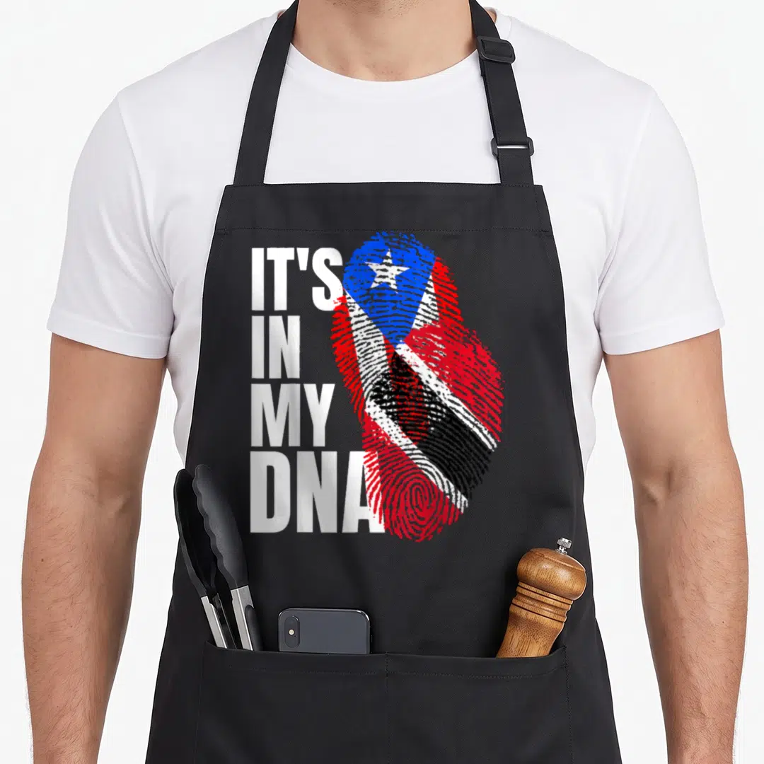 Boricua heritage aprons - Stacked white text IT'S IN MY DNA next to fingerprint filled with red white blue flag pattern — shown on a black cotton canvas apron against a white background