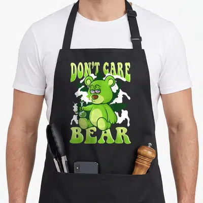 Stoned smoking apron - Lime green bear holding bong with don't care bear text and cannabis leaves — shown on a black cotton canvas apron against a white background