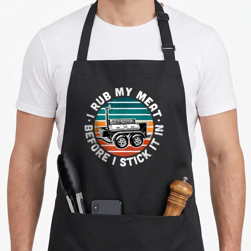 Offset meat aprons - Black smoker on teal orange and white stripes with pun text — shown on a black cotton canvas apron against a white background