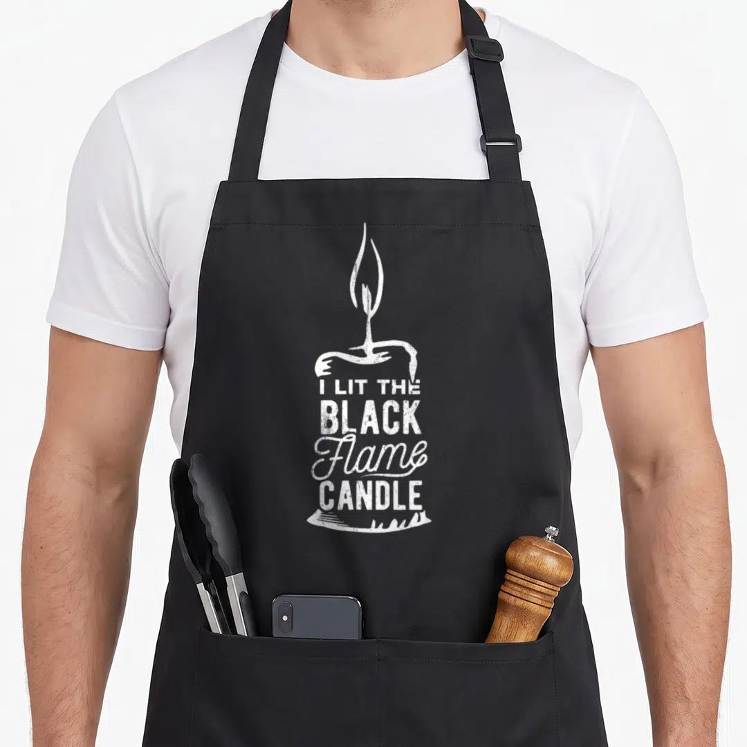 Lit halloween apron - White distressed candle illustration with I LIT THE BLACK Flame CANDLE text overlay — shown on a black cotton canvas apron against a white background