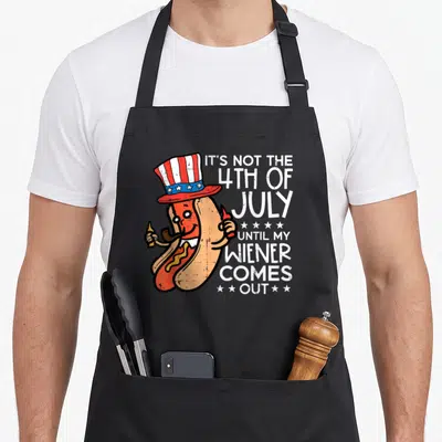 Wiener 4th of july apron - Cartoon hot dog in patriotic hat holding mustard and pipe with white pun text — shown on a black cotton canvas apron against a white background