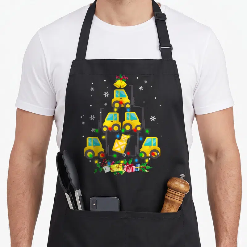 Forklift womens christmas aprons - Five yellow forklifts stacked as a Christmas tree with bells, lights, and holly — shown on a black cotton canvas apron against a white background