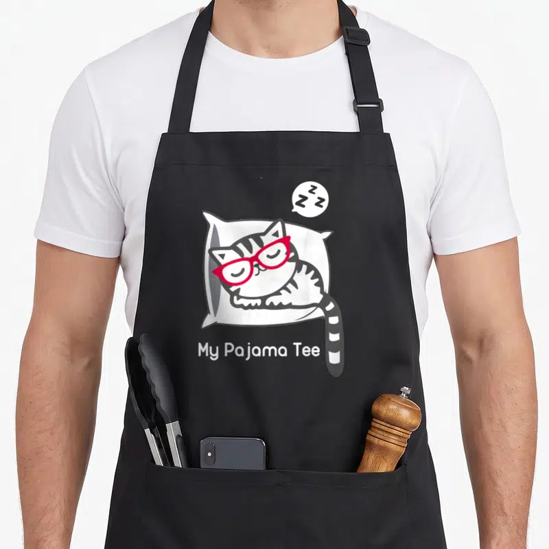 Pajama kitty cat apron - Sleeping grey cat with red glasses on white pillow, Zs bubble, My Pajama Tee text below — shown on a black cotton canvas apron against a white background