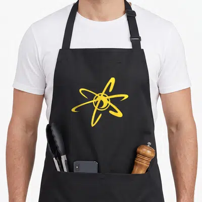 Jimmy cartoon apron - Yellow stylized atom symbol with intersecting elliptical orbits on grey background — shown on a black cotton canvas apron against a white background