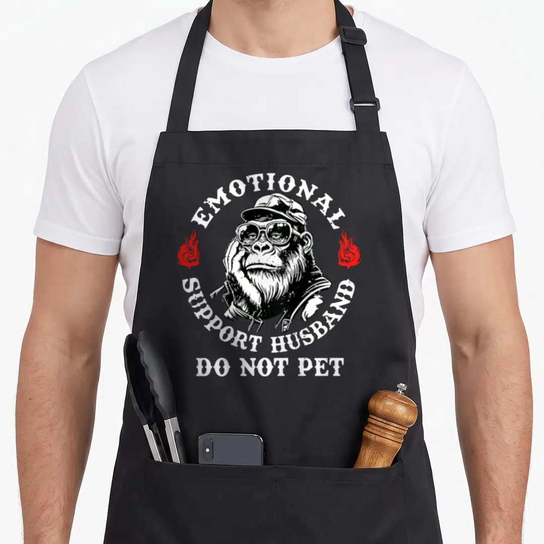Monkey husband apron - Chimpanzee in glasses and jacket with emotional support husband text and red flames — shown on a black cotton canvas apron against a white background