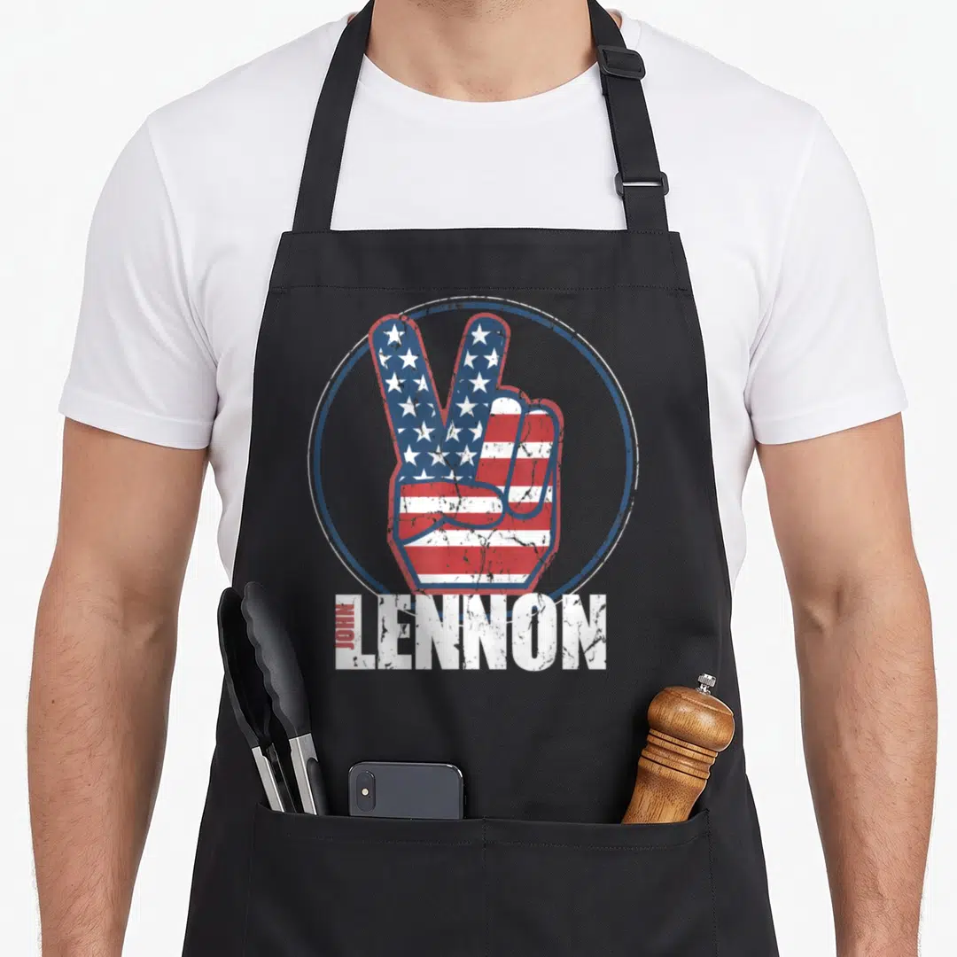 Blue john lennon apron - Red white blue peace sign hand filled with flag pattern and distressed JOHN LENNON text — shown on a black cotton canvas apron against a white background