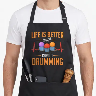 Workout gym class apron - LIFE IS BETTER with CARDIO DRUMMING text above three colored balls in buckets and drumsticks — shown on a black cotton canvas apron against a white background