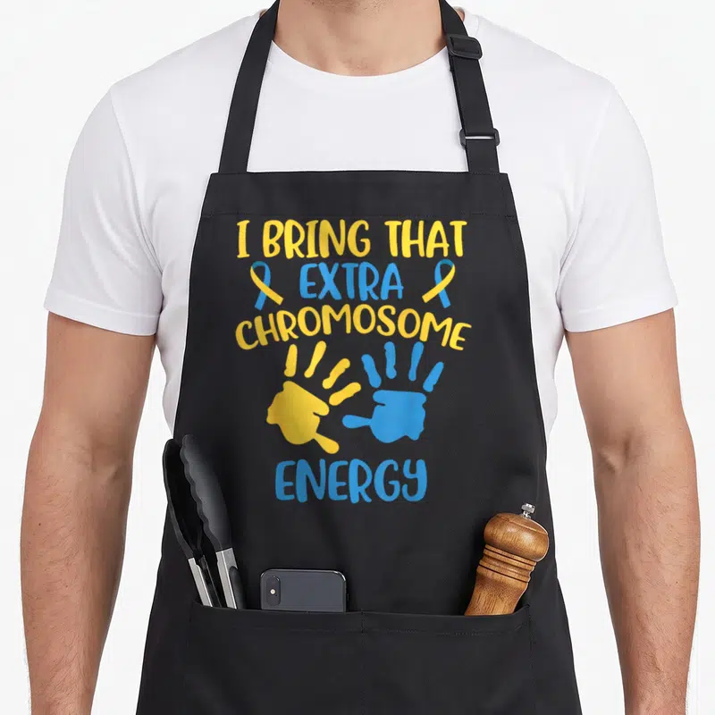 Chromosome an extra apron - I Bring That Extra Chromosome Energy text with yellow blue handprints and ribbons — shown on a black cotton canvas apron against a white background