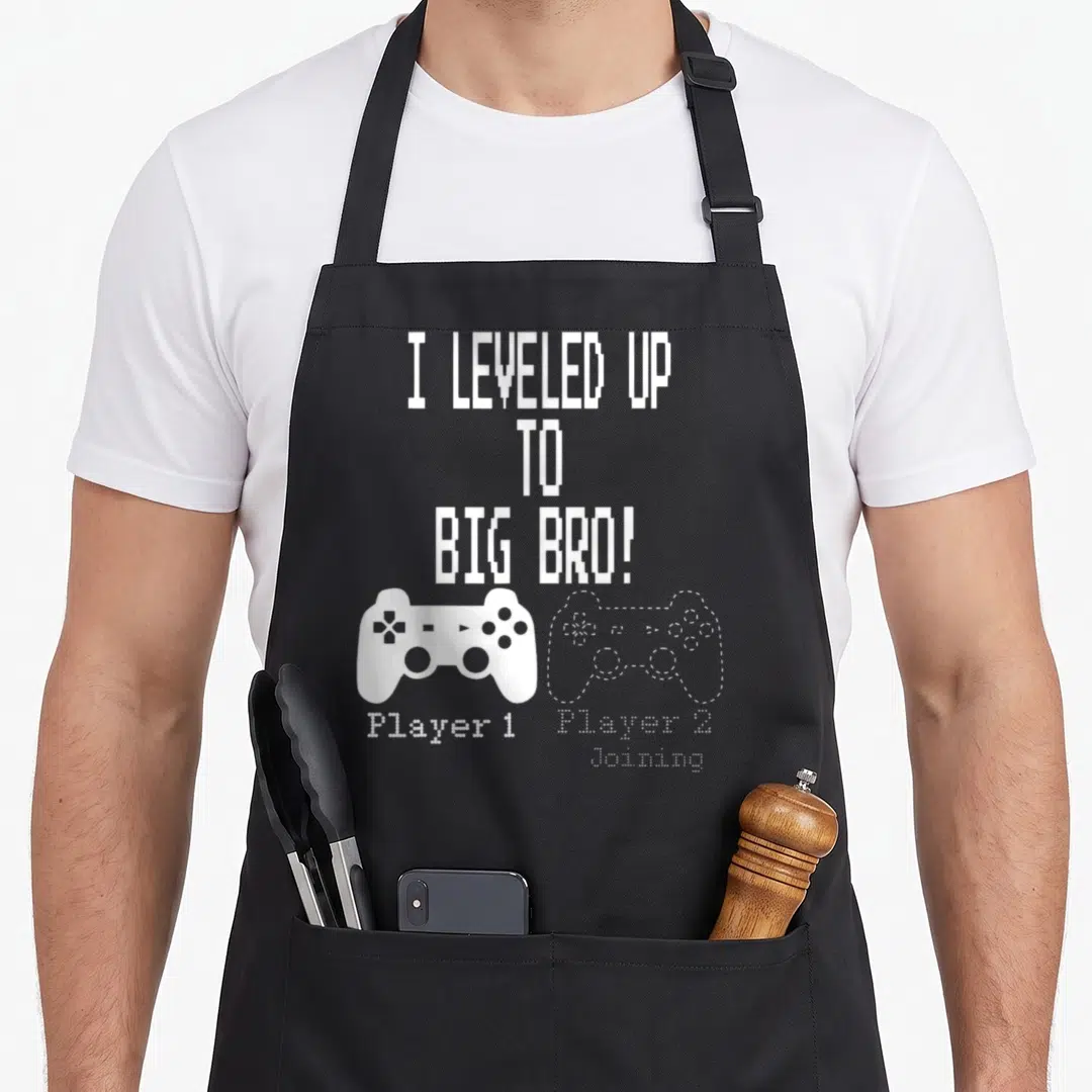 Leveled novelty apron - White pixelated text and two game controllers labeled Player 1 and Player 2 Joining — shown on a black cotton canvas apron against a white background
