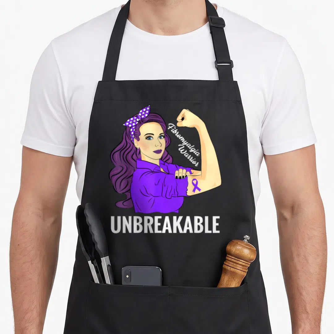 Fibromyalgia strong woman apron - Purple hair woman flexing arm with Fibromyalgia Warrior text and UNBREAKABLE below — shown on a black cotton canvas apron against a white background